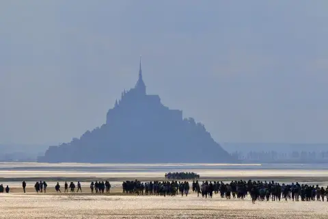 Silhouetten von Menschen auf dem Wattboden, die sich dem majestätischen Mont Saint-Michel nähern.